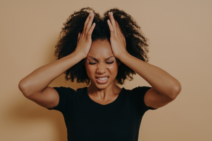 Black woman with both hands flat, rubbing the corners of her forehead and making a face of stress and anger.