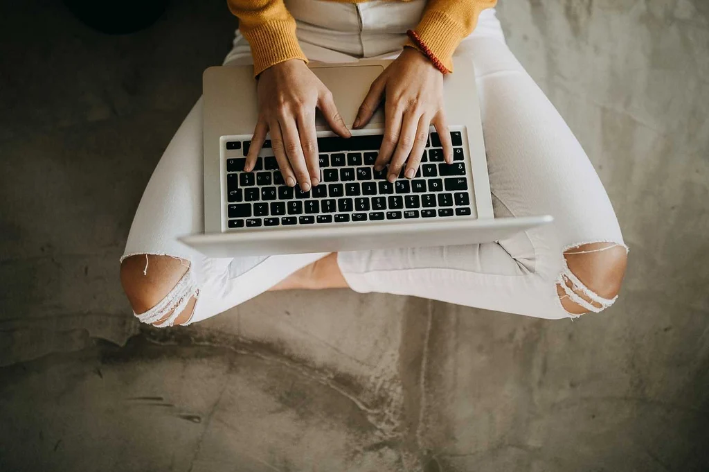Woman's hands typing on a laptop. The image illustrate "how to do a target audience research."