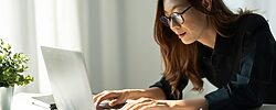 Asian woman typing on a laptop. The image illustrate a self-employed worker who makes a living as a freelance writer.