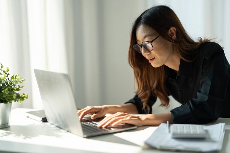 Asian woman typing on a laptop. The image illustrate a self-employed worker who makes a living as a freelance writer.