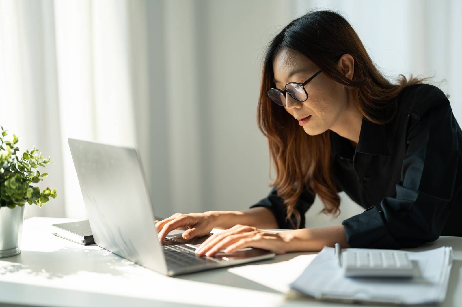 Asian woman typing on a laptop. The image illustrate a self-employed worker who makes a living as a freelance writer.