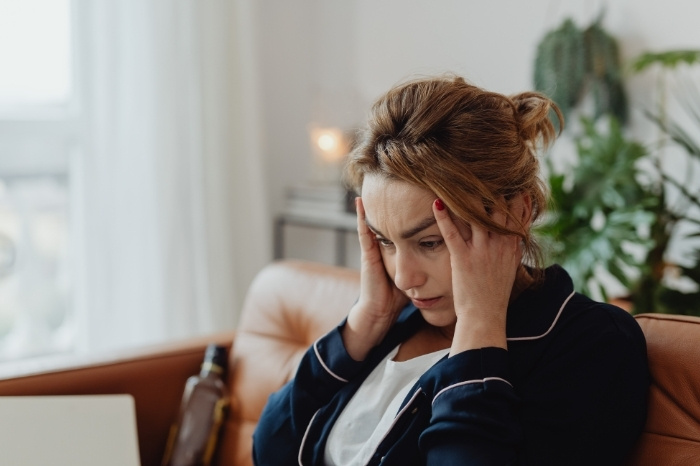 A woman touches her head with both hands, she looks tired and frustrated.