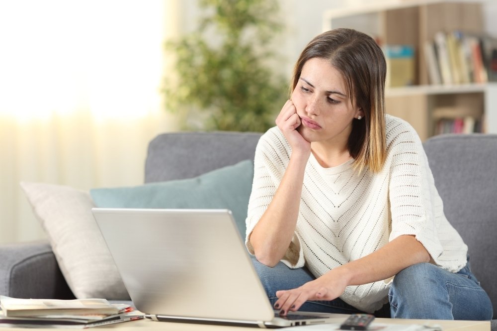 Woman wearing a white shirt and jeans stares in frustration to a laptop.