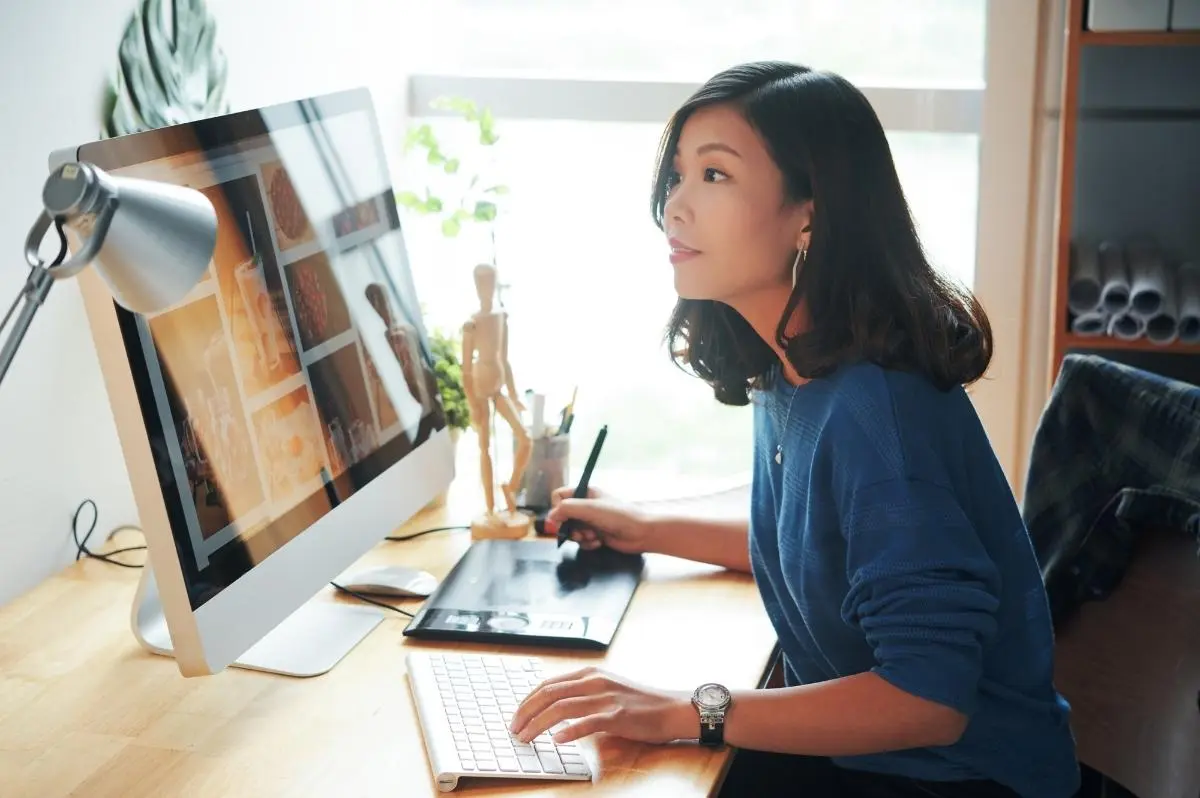 Young Asian woman working on her graphic design set up. The image illustrates the subject: "Why Graphic Designers need their own website."