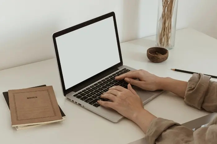 Person writing on a laptop in clean, white room.