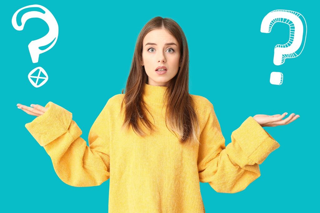 Woman in a yellow sweater, in front of a light blue background, expressing doubt with her face and arms.