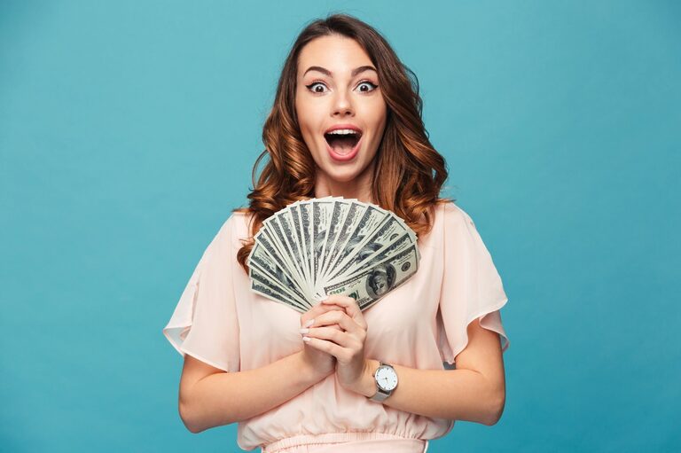 Long-haired woman wearing a pink dress, smiling, and holding money in a blue background.