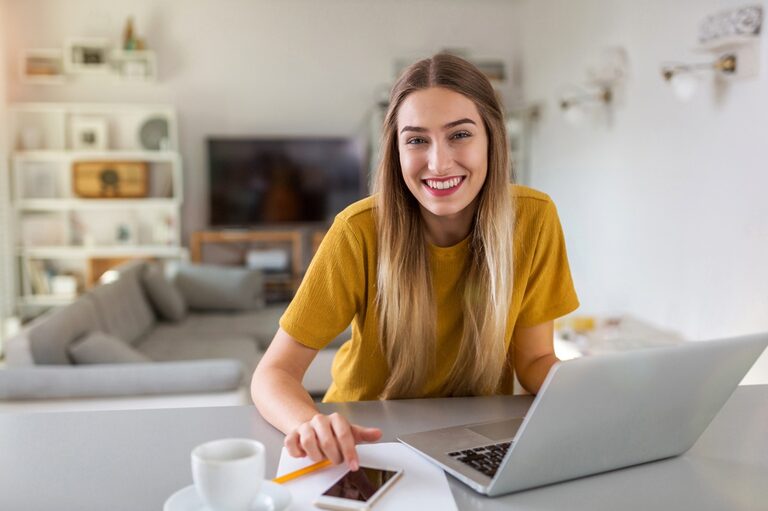 Blonde woman wearing a dark yellow t-shirt and working from home.