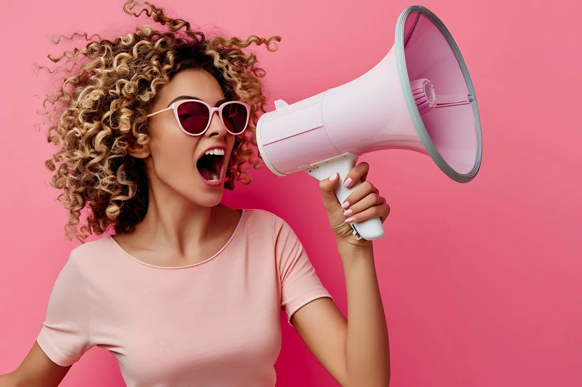 A black woman wearing a pink t-shirt and holding a pink megaphone in a pink background.