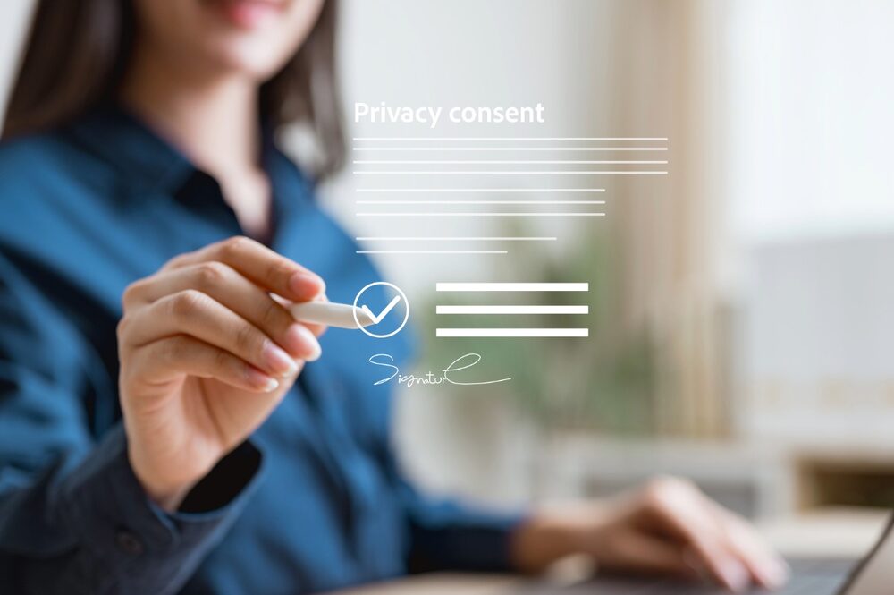 A woman in a blue shirt signs in mid-air, where a digital illustration of a contract with the words "privacy consent" suggests the issue of online security.