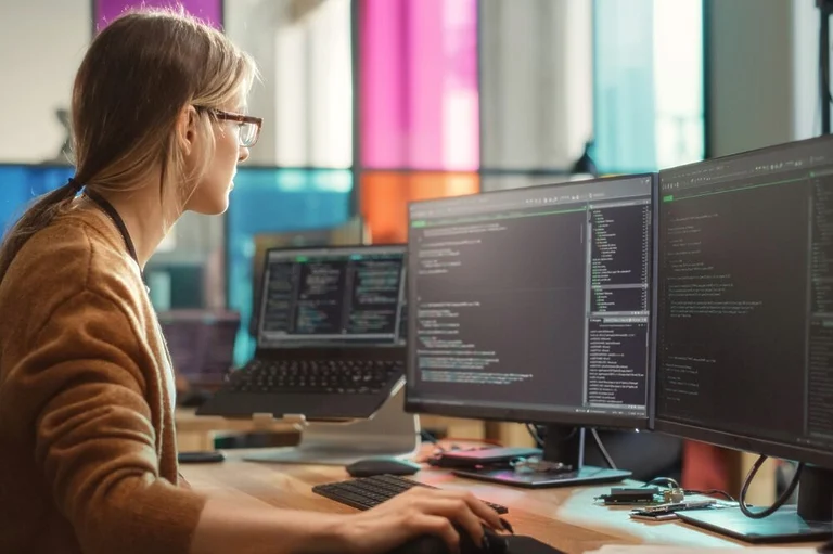 A person manipulating two desktop screens and one laptop screen displaying snippets of code.