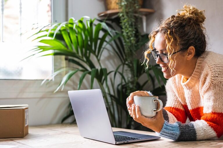 A woman holding a mug and smiling excitedly while looking at a computer screen.