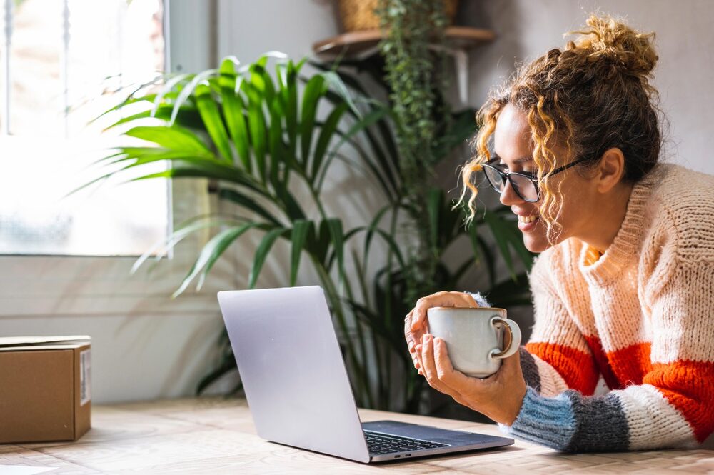 A woman holding a mug and smiling excitedly while looking at a computer screen.