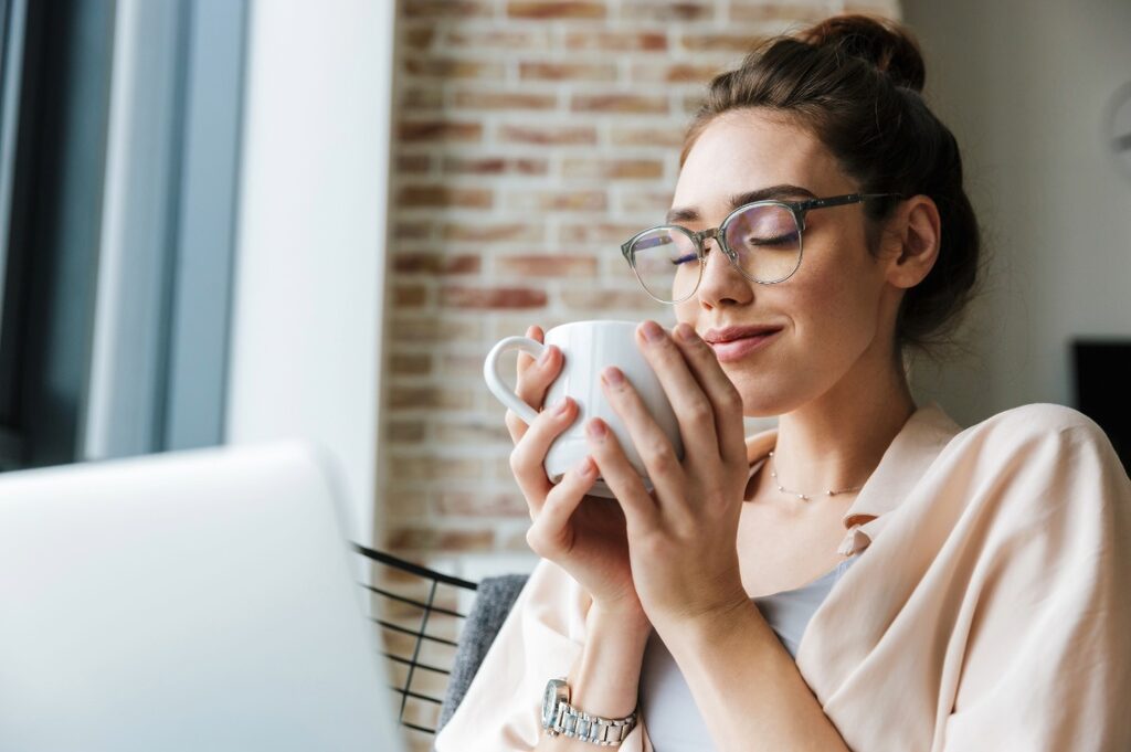Happy woman holding a cup of coffee while working from home.