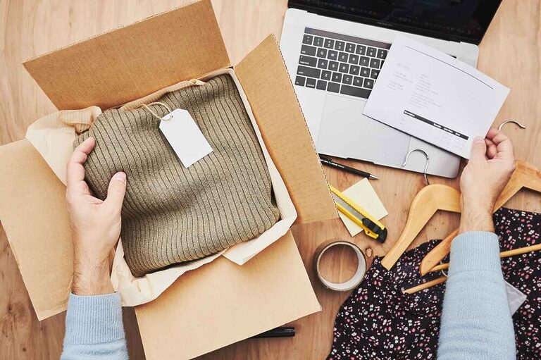 A person wrapping a package and checking shipping details on a computer screen.