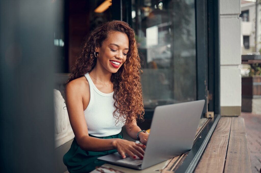 Young black woman blogging on a coffee shop, she's typing on her laptop.