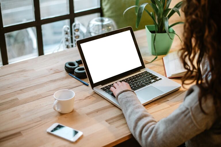 The image shows a long-haired woman working on a laptop on a coffee shop. The space has a cozy modern industrial vibe.