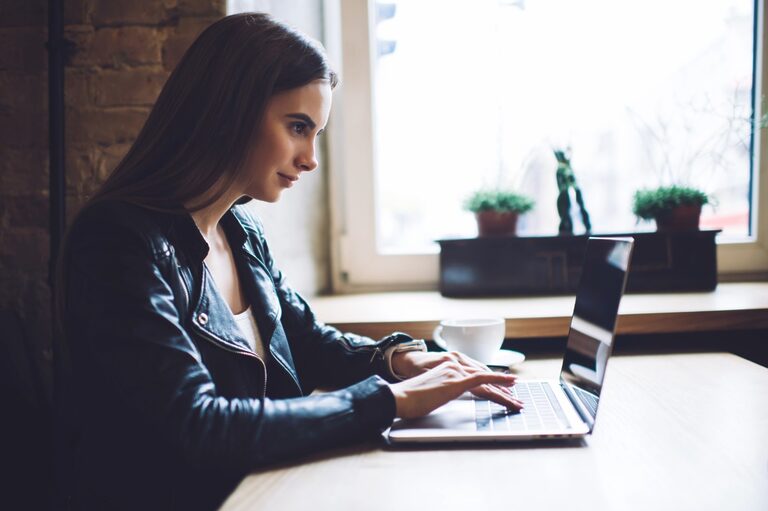 Woman wearing a leather jacket and browsing on a laptop.