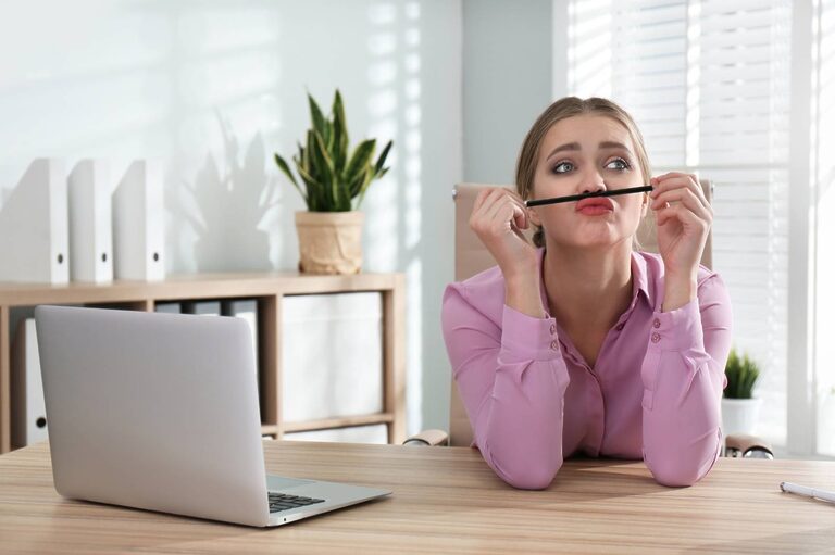 A woman rests a pencil on her upper lip, ignoring her laptop. She's having trouble focusing because she's multitasking.