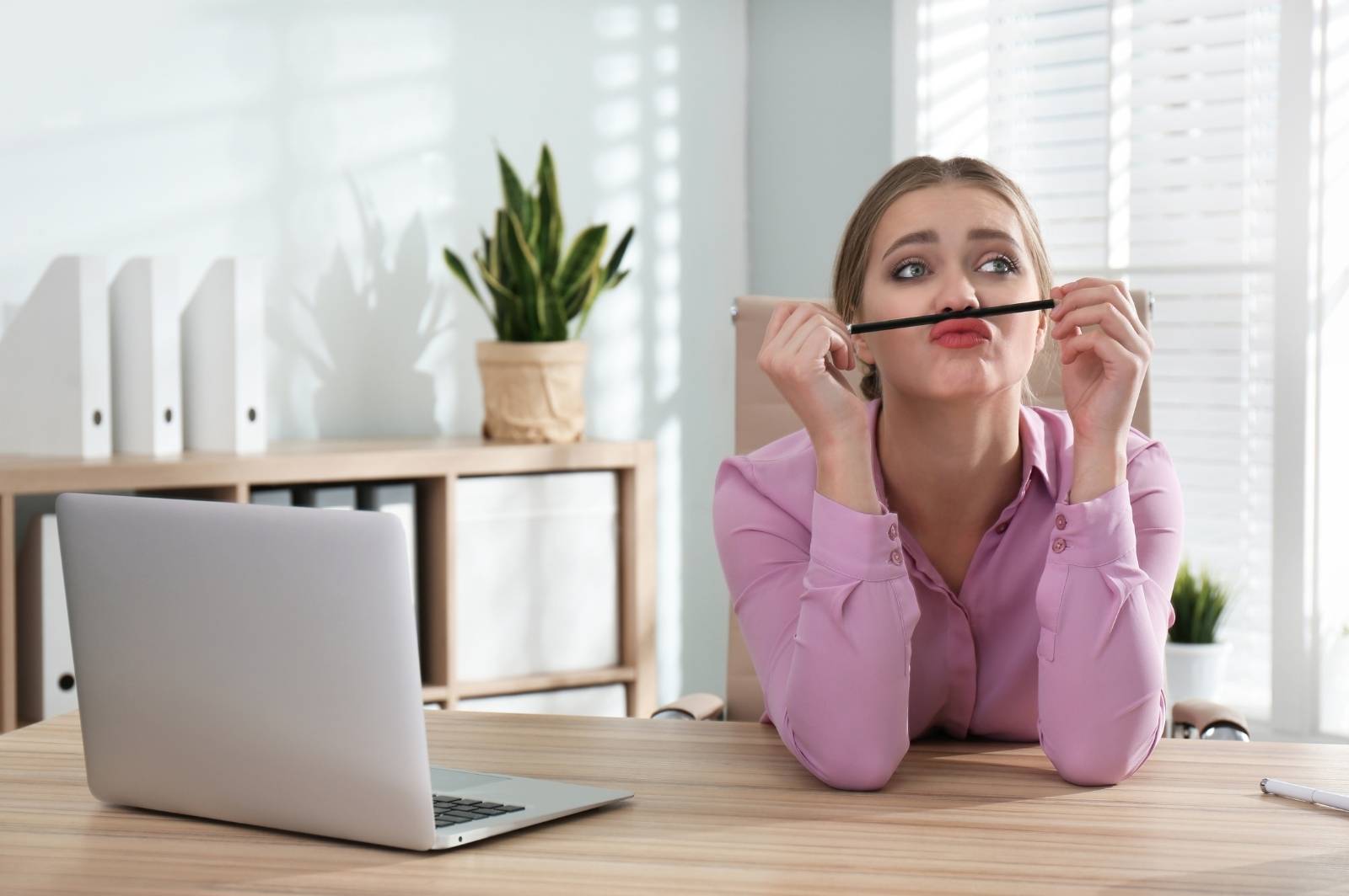 A woman rests a pencil on her upper lip, ignoring her laptop. She's having trouble focusing because she's multitasking.