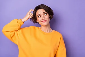 A woman scratches her head, expressing doubt. She is wearing a yellow blouse against a lilac background.