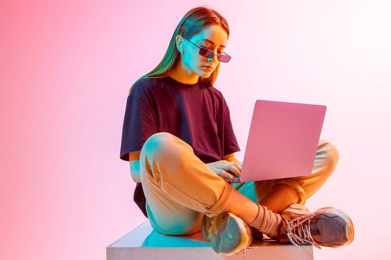 Modern pinkish neon light shining on a woman sitting with a laptop on her legs.
