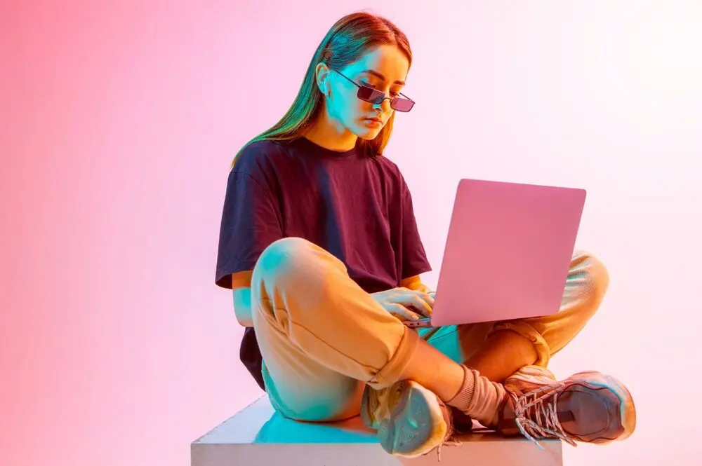 Modern pinkish neon light shining on a woman sitting with a laptop on her legs.
