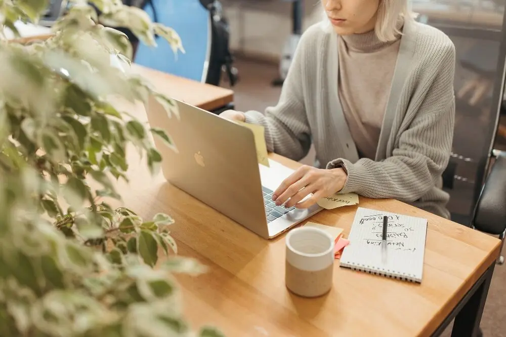 Woman working on a coworker space, using a grey laptop and a notebook.