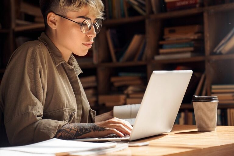A short-haired person wearing glasses to work with a laptop.