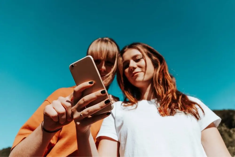 Two young women checking something on a smartphone screen in a sunny day.