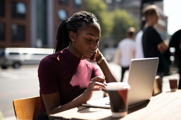 A black woman working with a laptop in an open-air coffee shop.