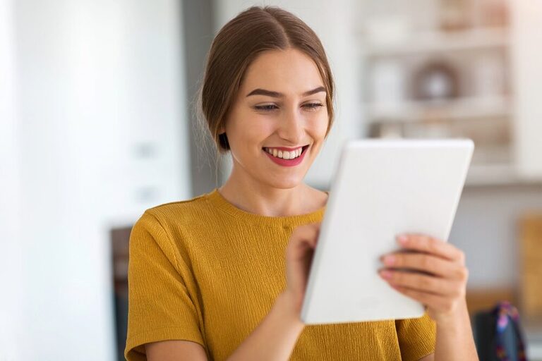 The image shows a woman with her hair tied back, engrossed in reading with her tablet in hand.