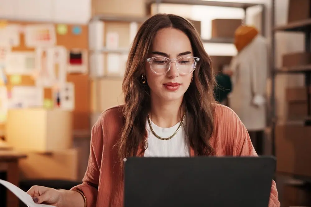 The image shows a woman concentrating, wearing glasses and working in front of a computer.